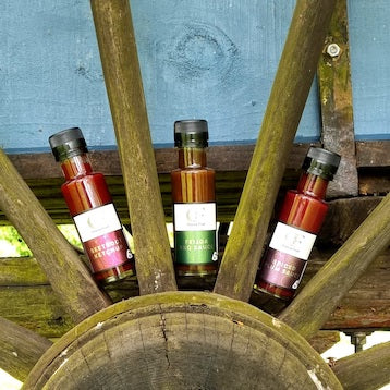 Three bottles of hot sauce on a wooden wheel with a blue background
