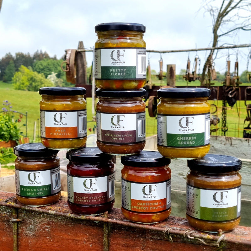 Assorted jars of Choice Fruit preserves on a wooden surface with a countryside background.