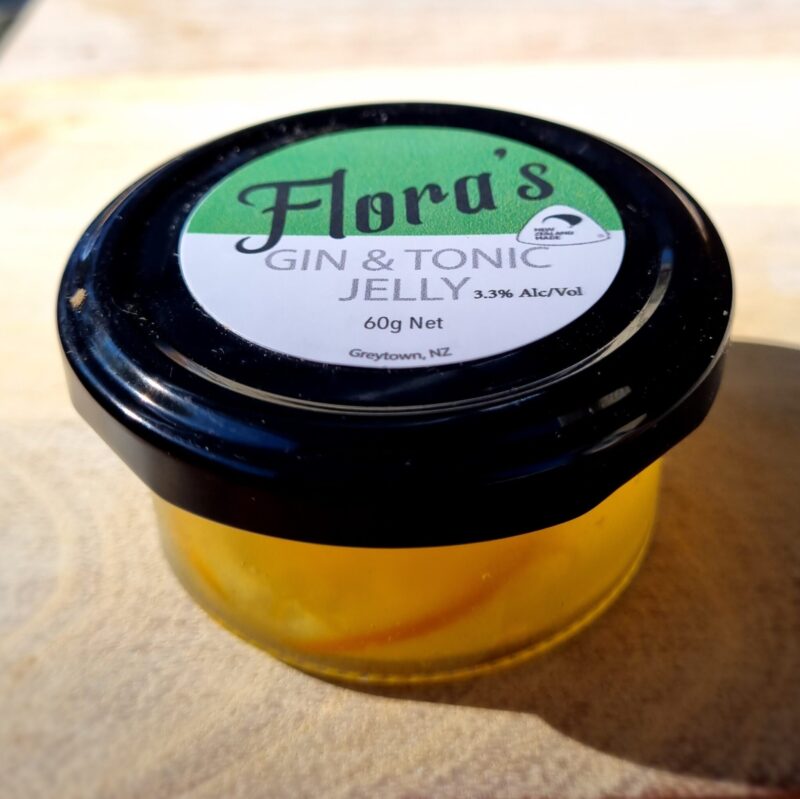 A jar of Flora's Gin & Tonic Jelly with a clear label showing the product name and the net weight of 60g. The jelly appears to be a bright yellow color.