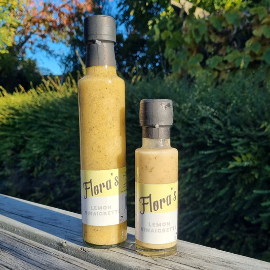 Two bottles of Flora's Lemon Vinaigrette on a wooden surface with a natural background.