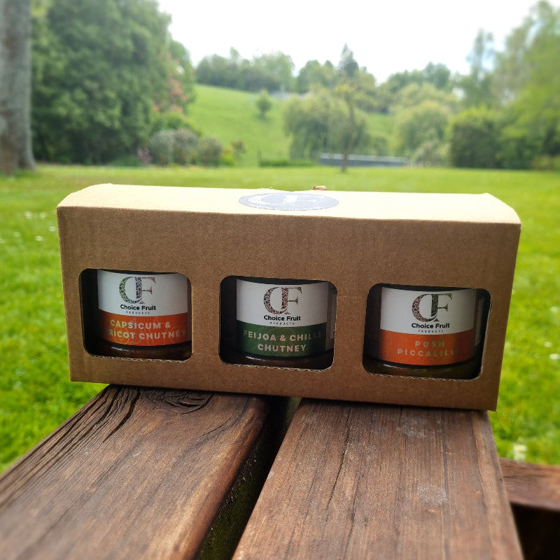 Three chutney jars in a cardboard box with a scenic background
