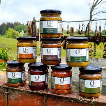 Assorted jars of Choice Fruit preserves on a wooden surface with a countryside background.