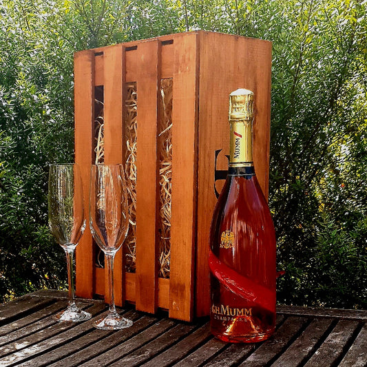 Bottle of Mumm champagne with two glasses in a wooden crate outdoors.