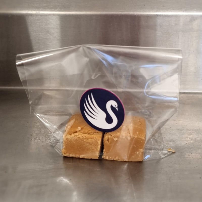 Block of fudge in a clear plastic bag with a swan logo on a metallic surface