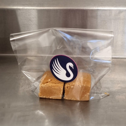Block of fudge in a clear plastic bag with a swan logo on a metallic surface