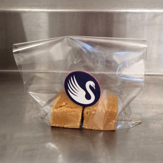 Block of fudge in a clear plastic bag with a swan logo on a metallic surface