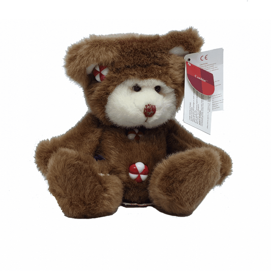 A plush teddy bear designed to look like a gingerbread man, with brown fur and white and red accents, sitting upright with a tag attached to its ear.